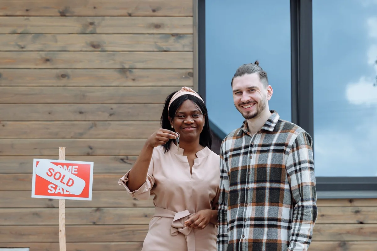 A smiling couple holding a new-home key outside a house.